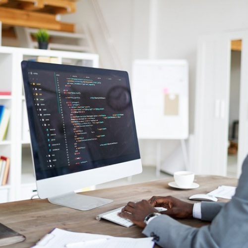 Young elegant software developer in formalwear sitting by desk in front of computer screen while decoding data